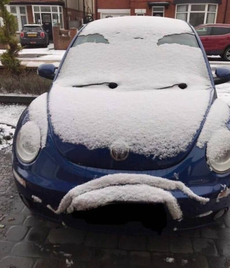 Car covered in snow with a snowman face on the front.