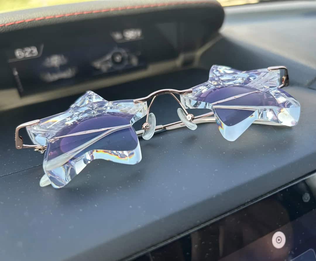 Sunglasses with star-shaped, iridescent lenses on a car dashboard.