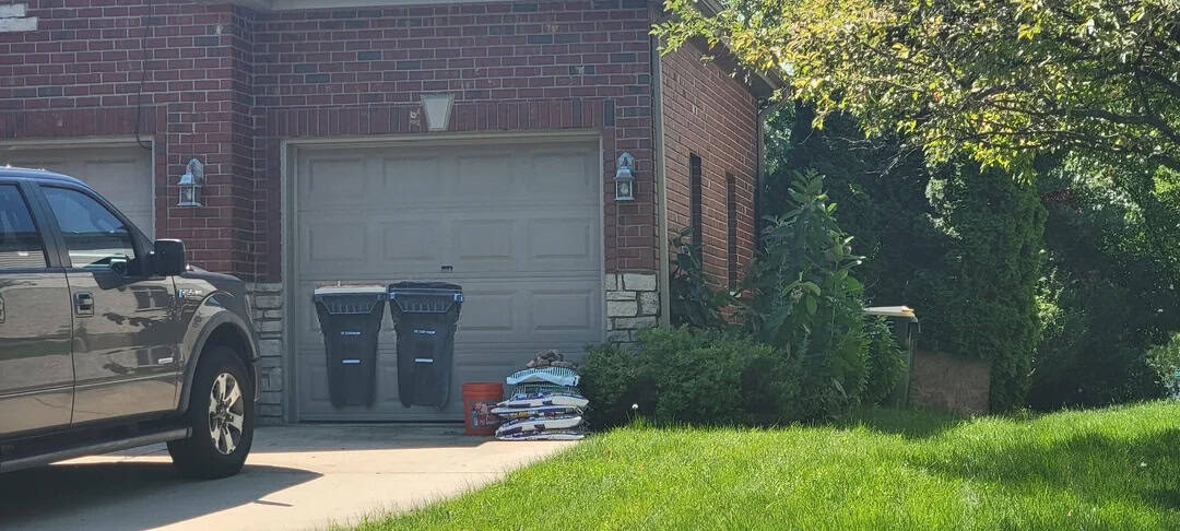 Garage with two blue trash bins and bags of yard waste outside.