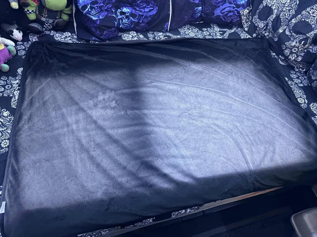 Black suitcase on bed with patterned bedding and purple pillows.