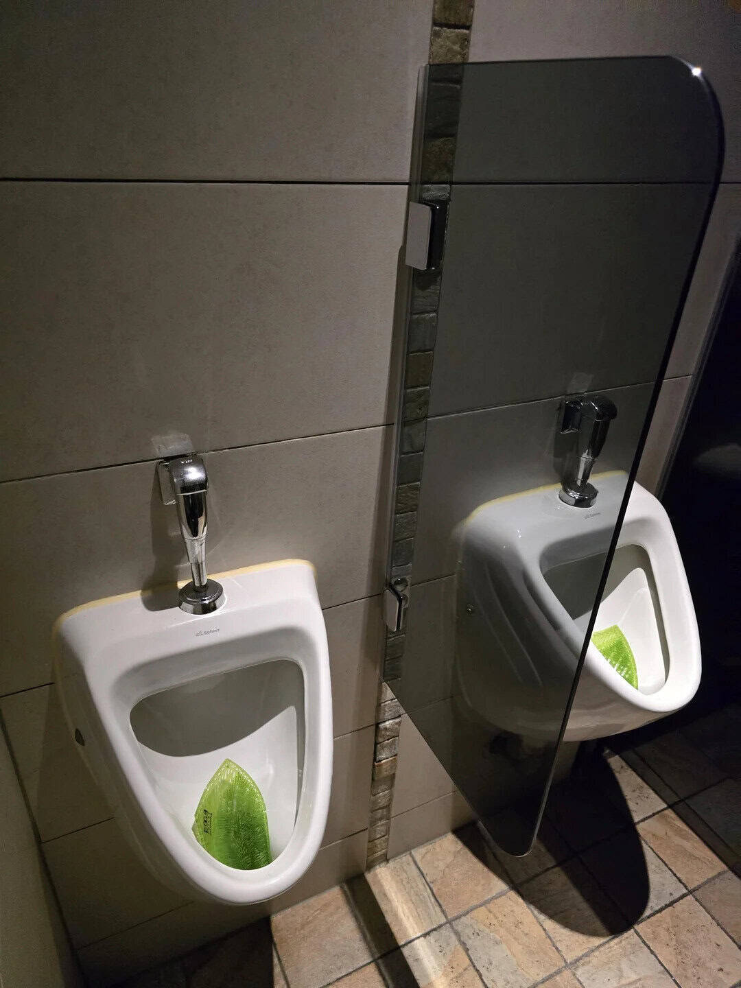 Urinals with a mirror reflecting one urinal in a bathroom.