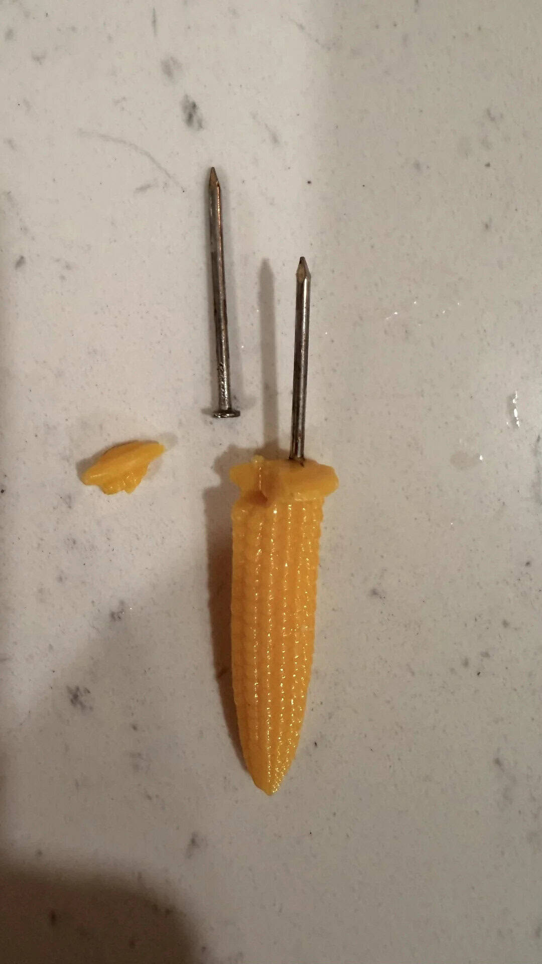 A piece of yellow cheese with two sewing pins stuck in it on a white surface.