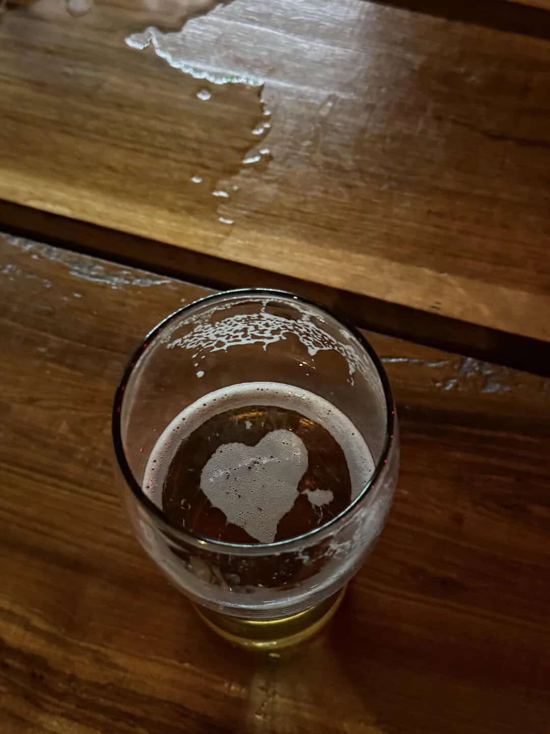 Heart-shaped foam in a glass of beer on a wooden table.
