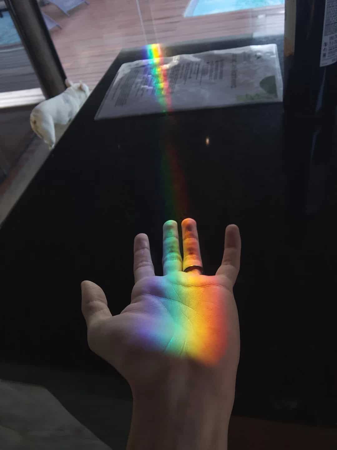 Hand with rainbow light reflection on fingers and palm, rainbow on table.