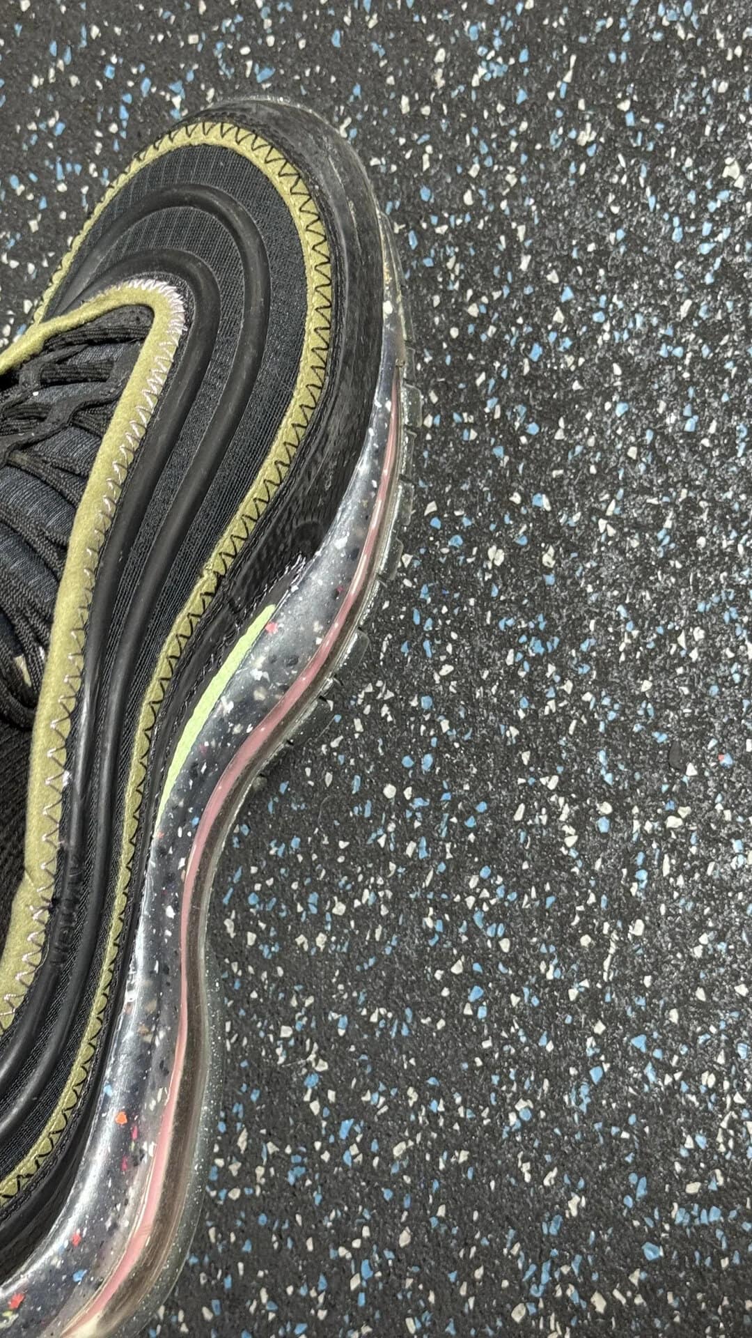 Close-up of a sneaker with a yellow and black design on a speckled gym floor.