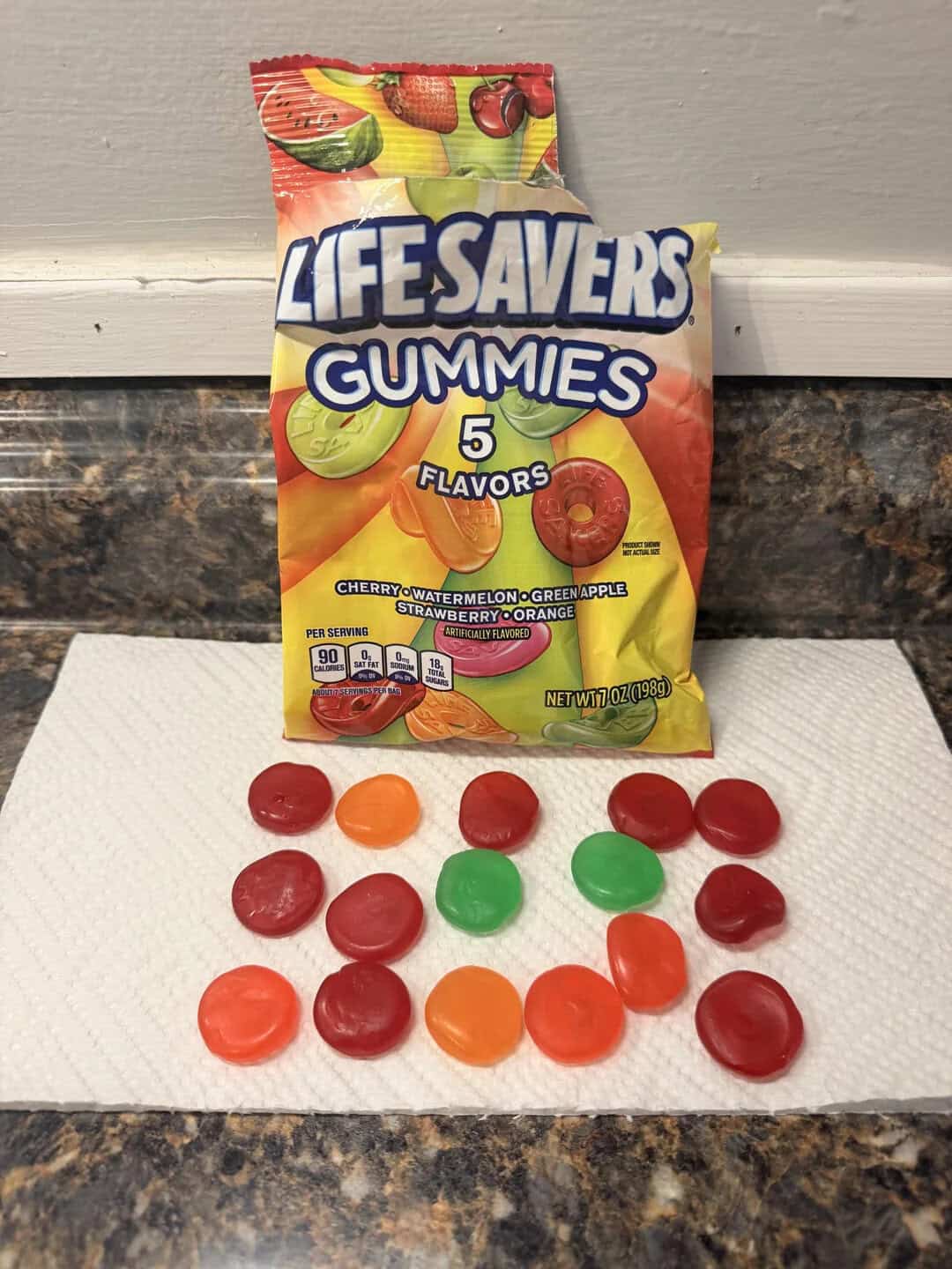 Lifesavers Gummies bag with assorted gummies in front on a white surface.
