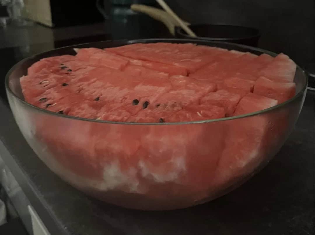 A large glass bowl filled with sliced watermelon on a dark surface.