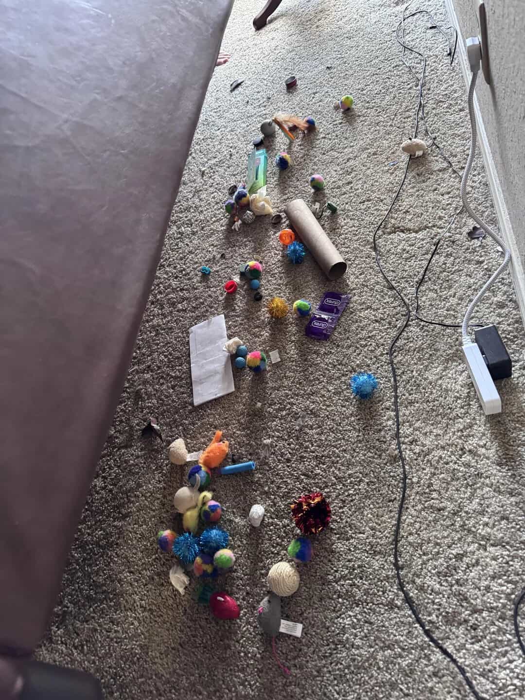 Messy carpet with scattered colorful toys, a cardboard tube, and electrical cords.