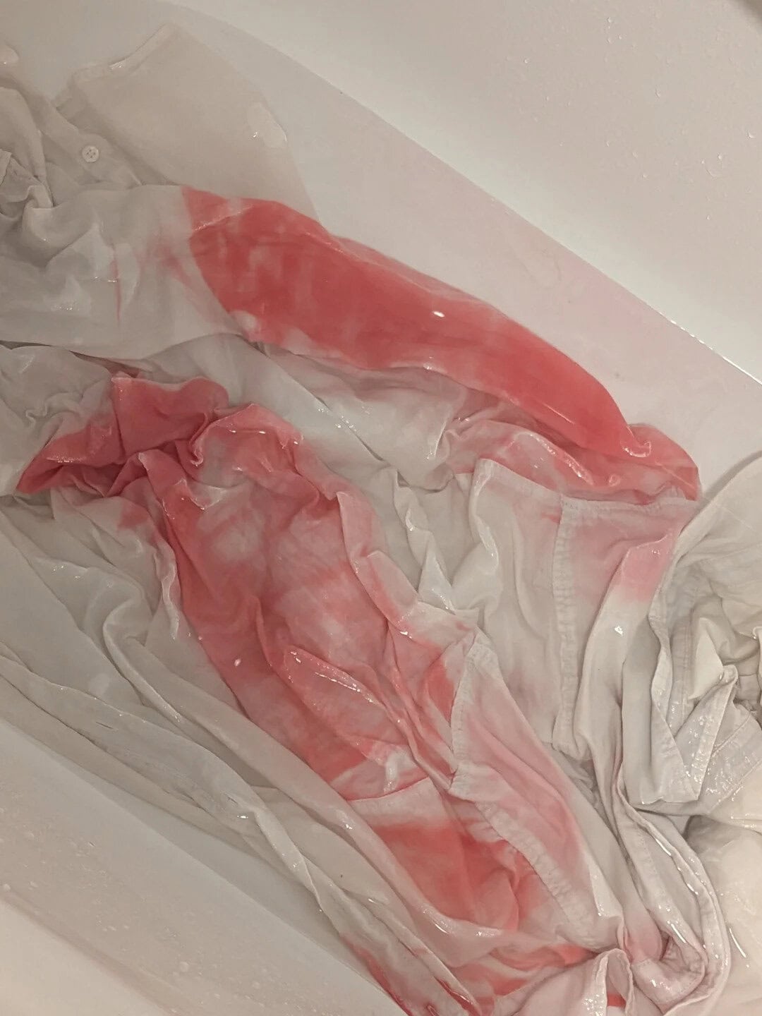 Crumpled white fabric with red and pink stains, possibly blood, in a plastic bag.
