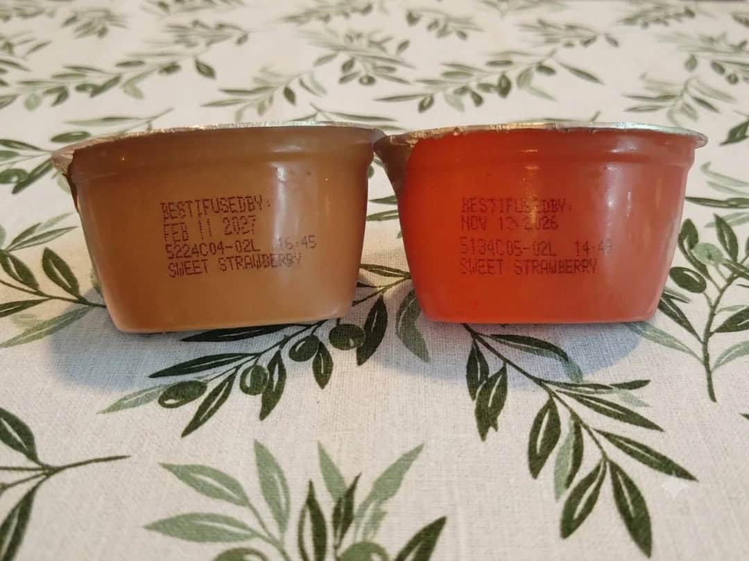 Two strawberry-flavored pudding cups, one chocolate and one strawberry, on a leafy tablecloth.