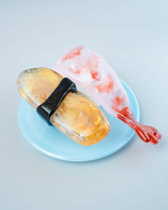 Glass food sculpture of a fish with a red tail on a blue plate.