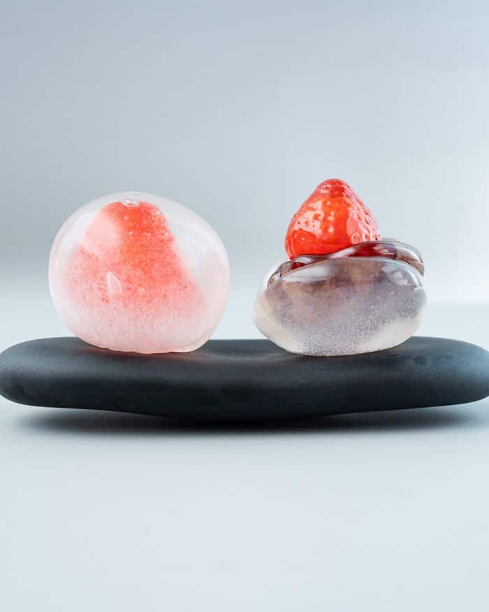 Glass food sculptures of a peach and a strawberry on a black base.