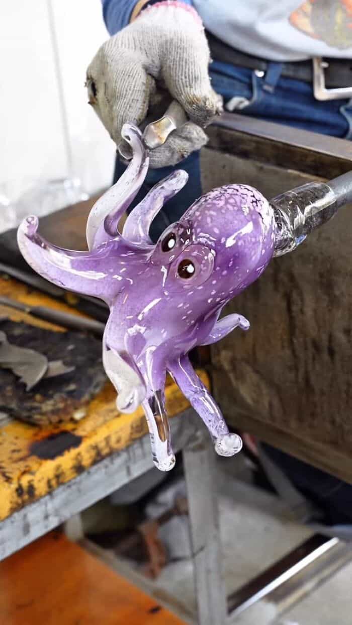 Colorful glass octopus sculpture being shaped by artist's hand.