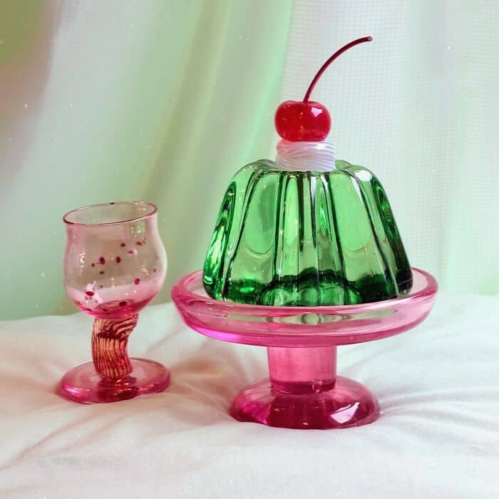 Colorful glass food sculptures with cherry on top, on a pink stand and a pink glass.