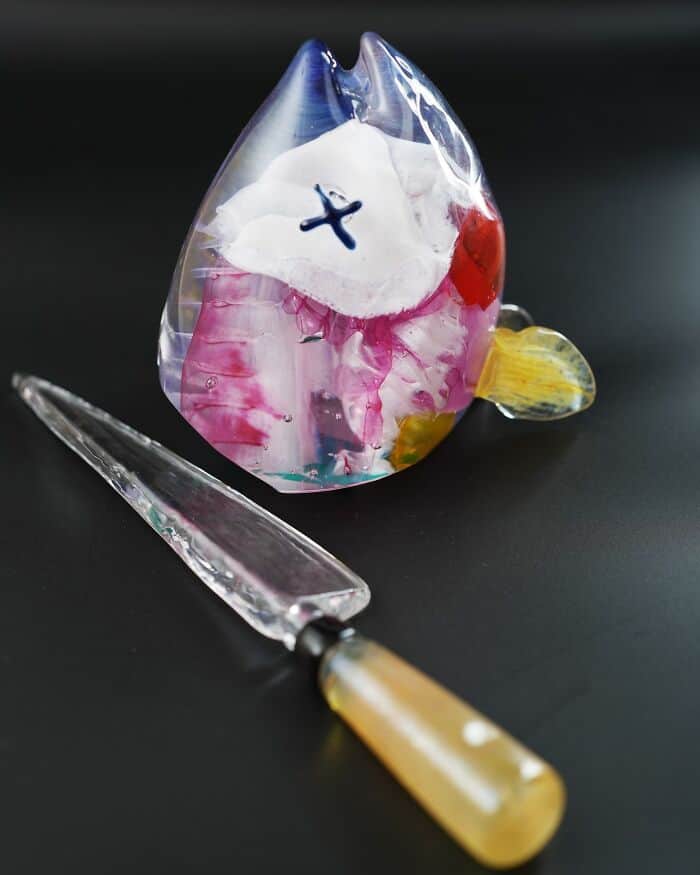 Colorful glass fish sculpture with a knife on a black background.