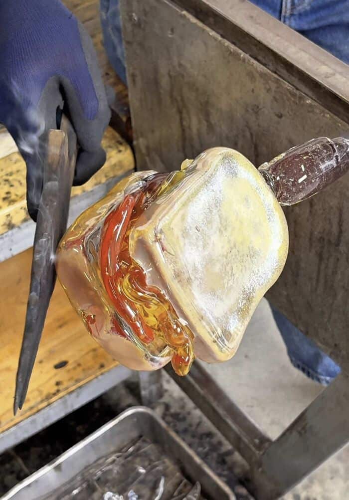 Molten glass being shaped by a craftsman with tools in a workshop.