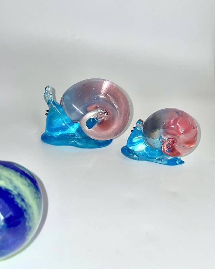 Glass snail sculptures in pink and blue on a white background.