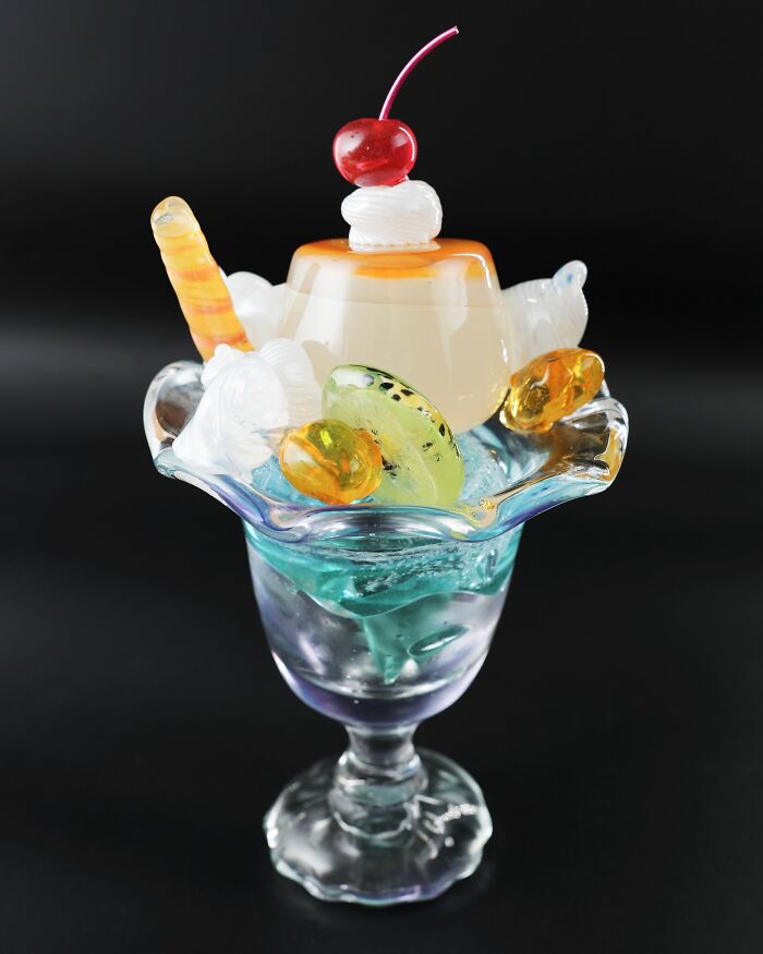 Glass sculpture resembling a dessert with cherry, whipped cream, and candies.