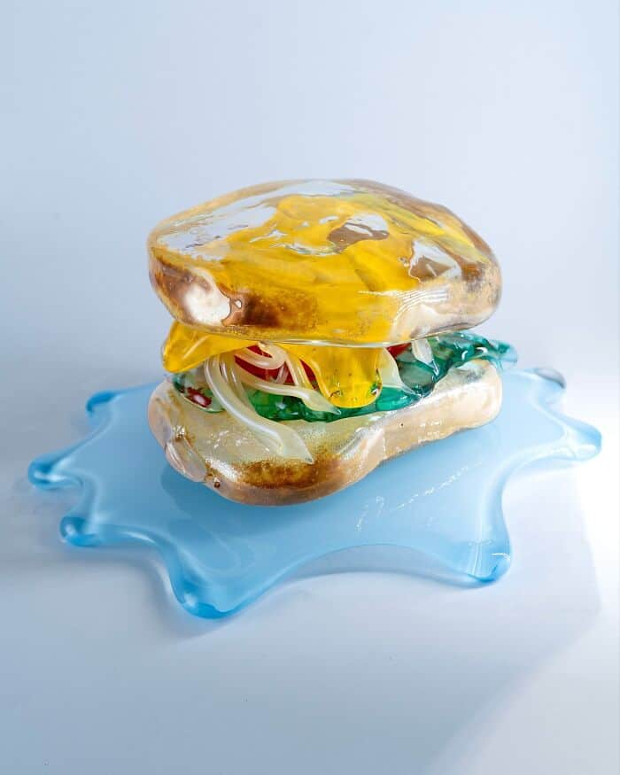 Glass food sculpture of a burger on a blue plate, by Miwa Ito.