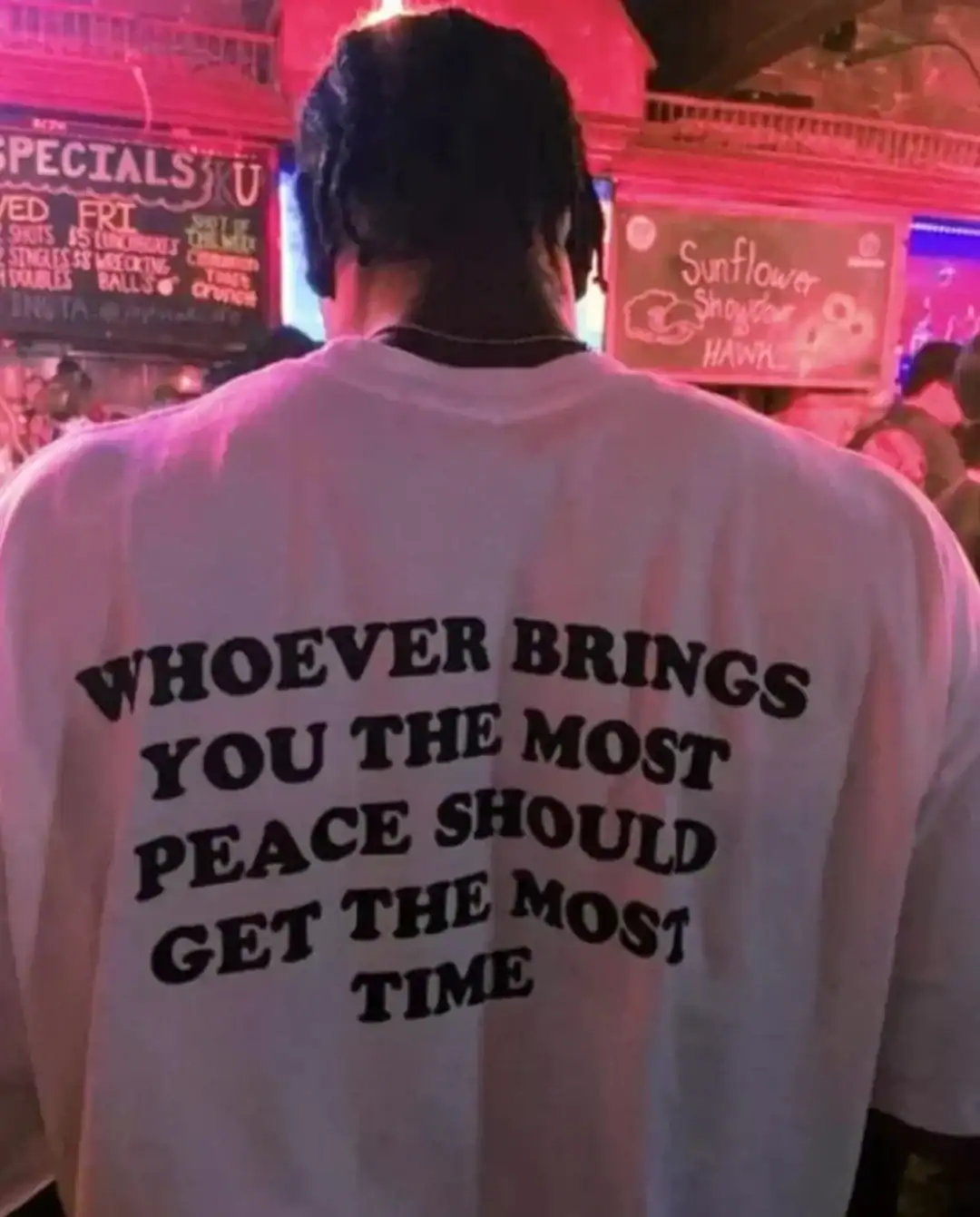 Person wearing a white shirt with a motivational quote in a neon-lit setting.