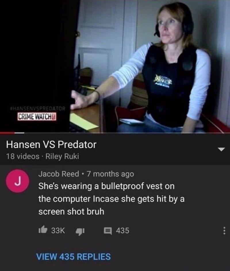 Woman with headphones at a desk, wearing a bulletproof vest, watching a computer screen.