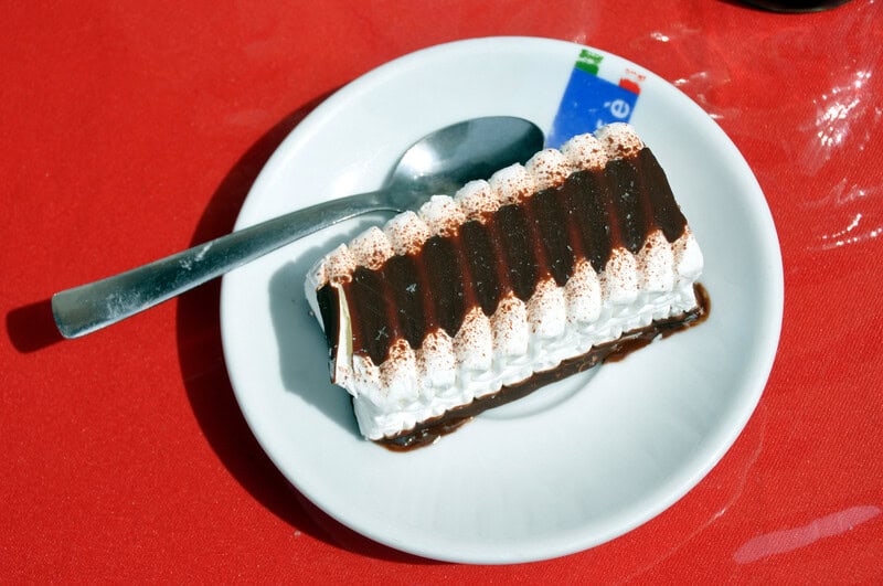 Chocolate and cream layered dessert on white plate with spoon, on red table.