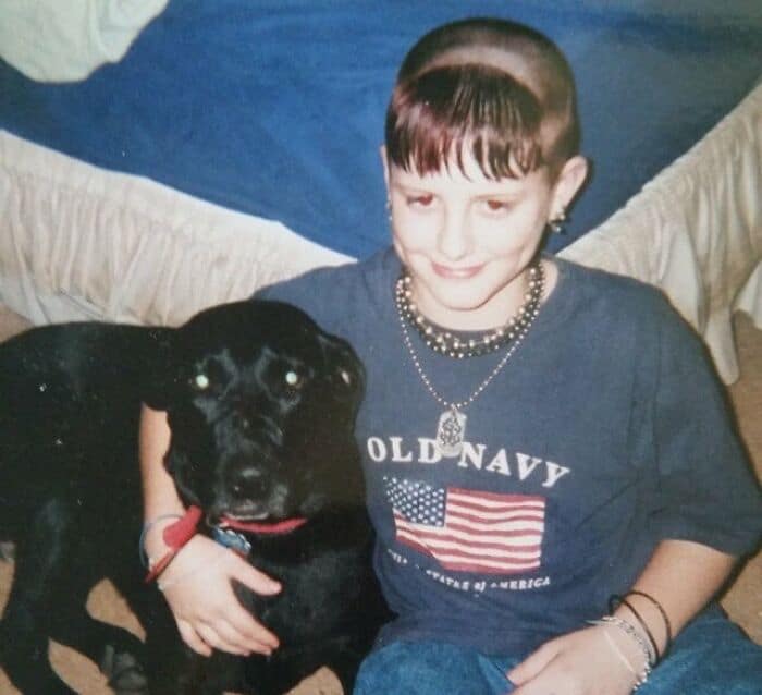 Girl with a short, straight haircut and a black dog, both sitting on a bed.