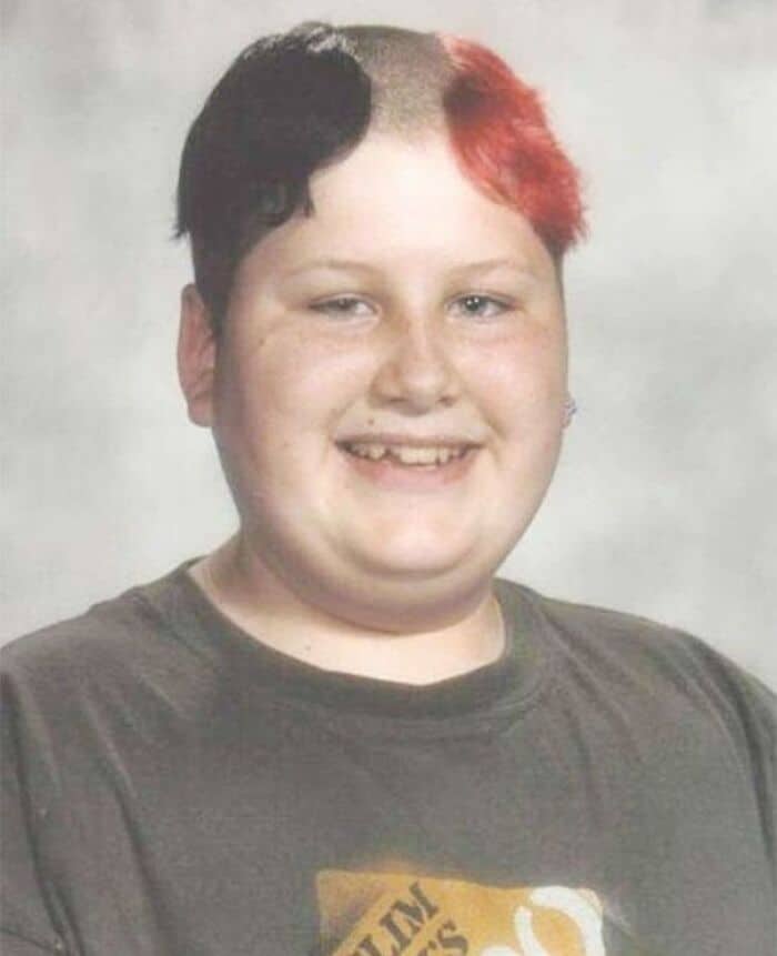 Child with black and red hair, smiling, in a gray T-shirt.