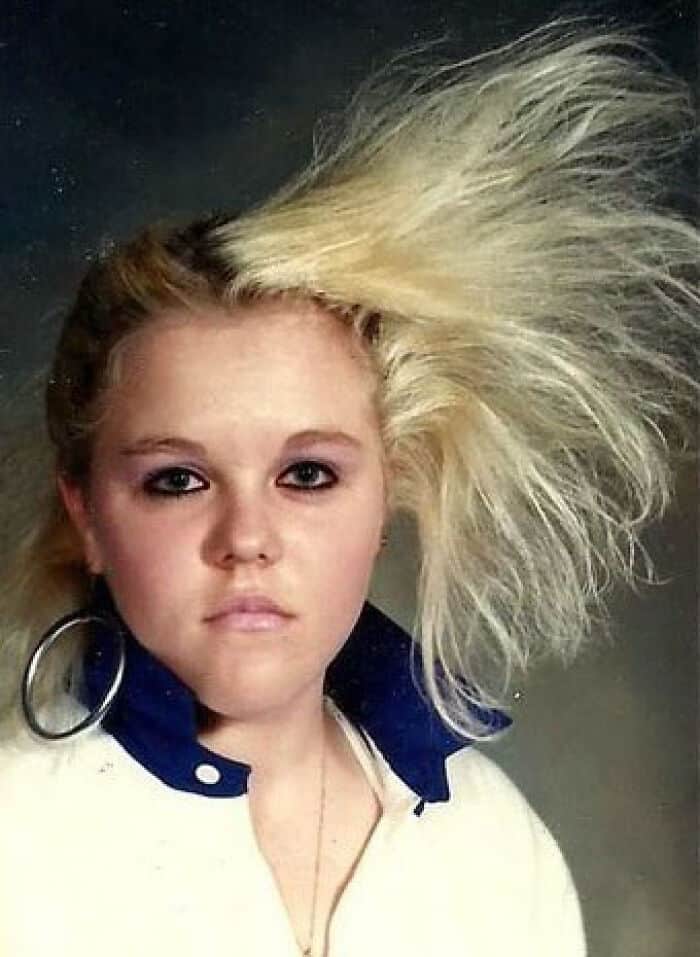 Young girl with big blonde hair styled in a dramatic fashion, wearing large hoop earrings.