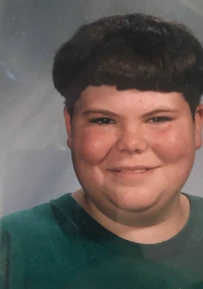 Child with a bowl haircut, smiling, wearing a green shirt.