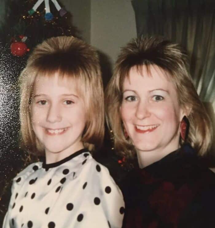 Two women with 80s/90s hairstyles smiling, Christmas tree in background.