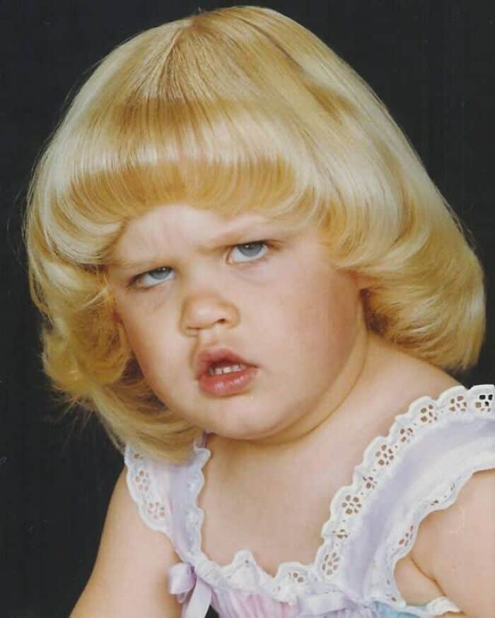 Child with a funny 80s or 90s hairstyle, blonde hair, and a confused expression.