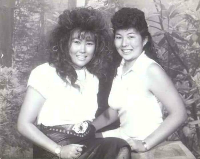 Two women with big, voluminous 80s hairstyles smiling outdoors.