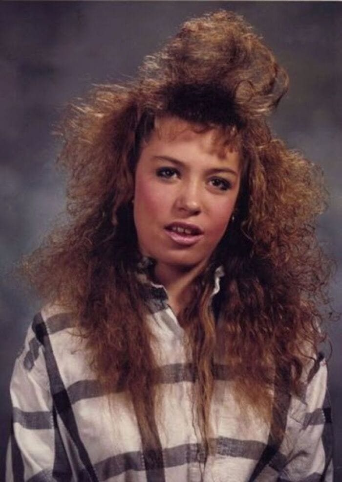 Young woman with big, teased, and voluminous 80s hairstyle, wearing a plaid shirt.
