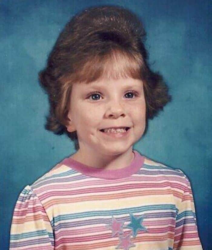 Child with big 80s/90s hairstyle and striped shirt, smiling.