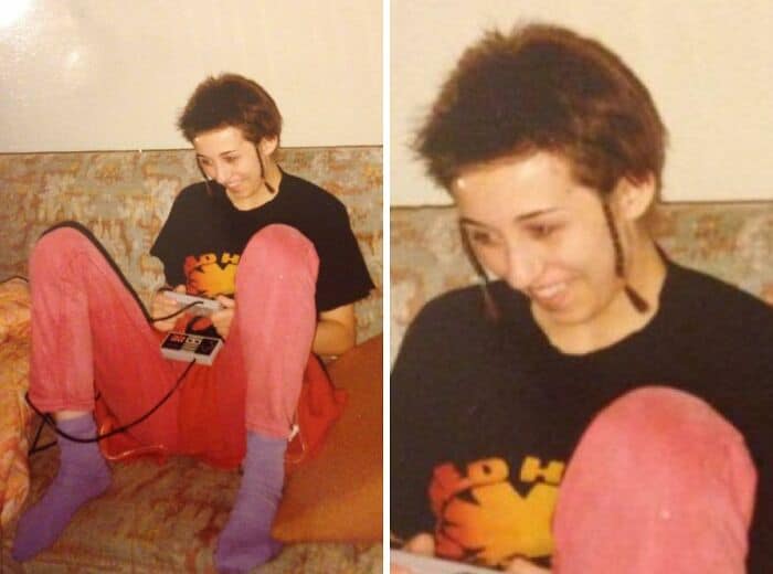 Young person with short, spiky hair, wearing a black T-shirt, pink pants, and purple socks, sitting.