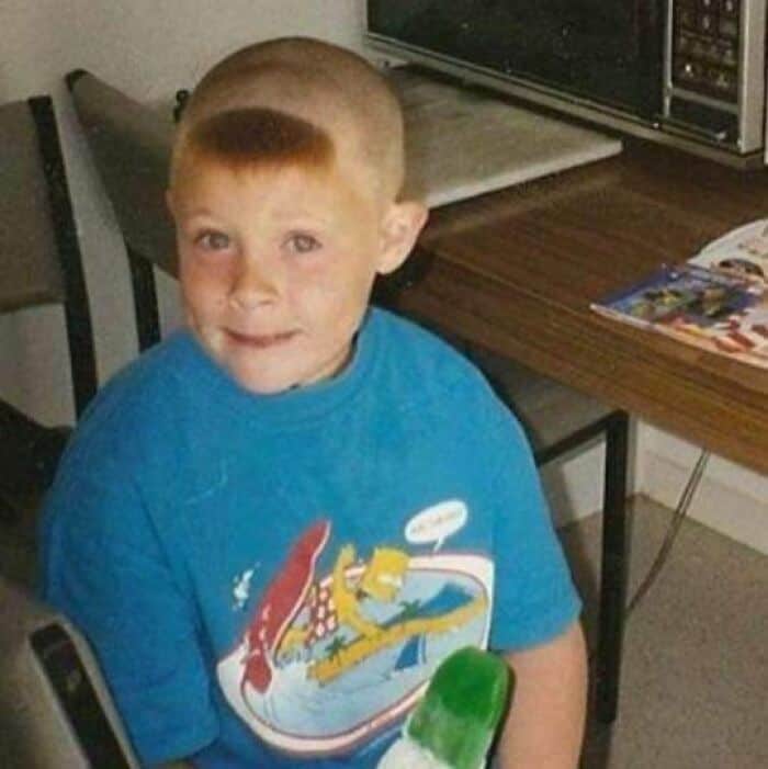Child with a unique, high, reddish-blonde haircut wearing a blue T-shirt.