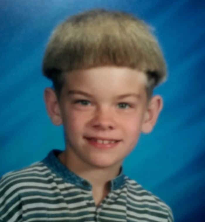 Child with a bowl haircut, smiling, wearing a striped shirt.
