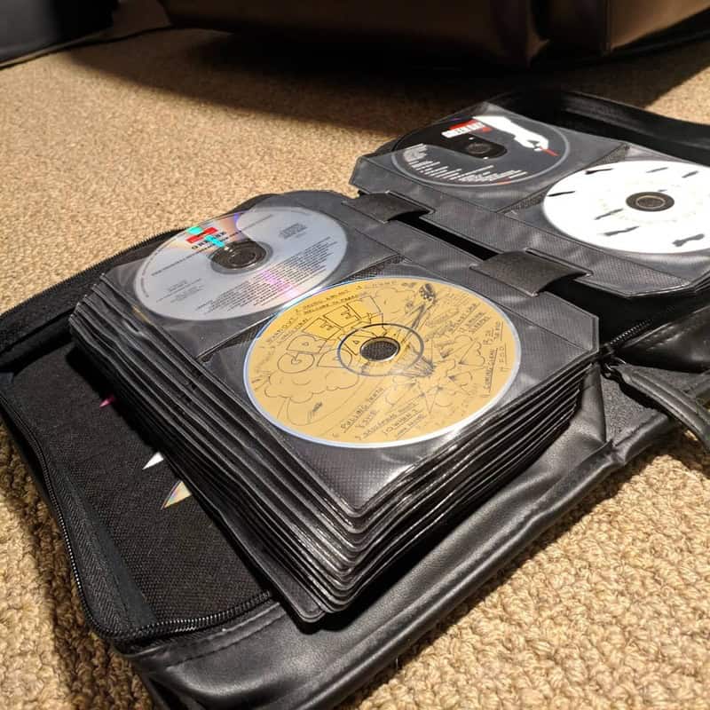 Stack of old CDs in a black case on carpet, with some discs visible.