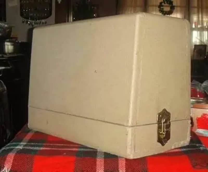 Vintage beige household storage box with brass latch on a red plaid tablecloth.