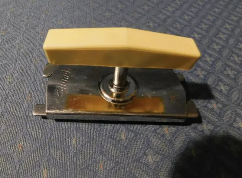 Vintage stapler with a beige top and metal base on a blue fabric surface.