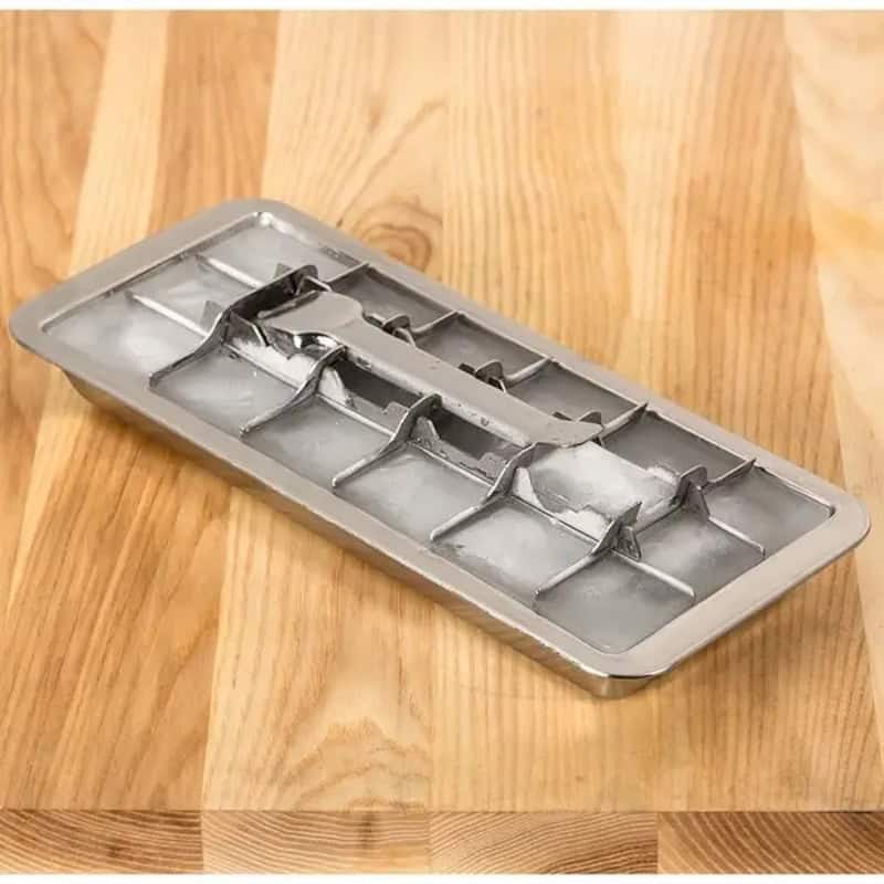 Vintage metal ice cube tray with compartments on wooden surface.
