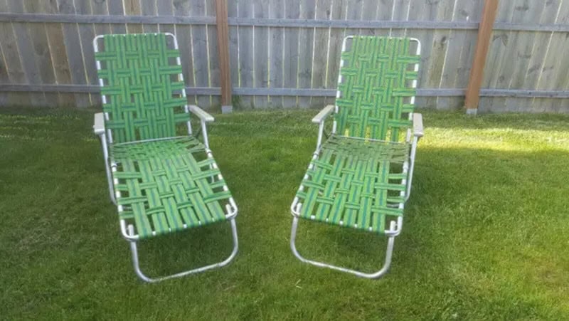 Two green lawn chairs with white frames on a grassy yard.