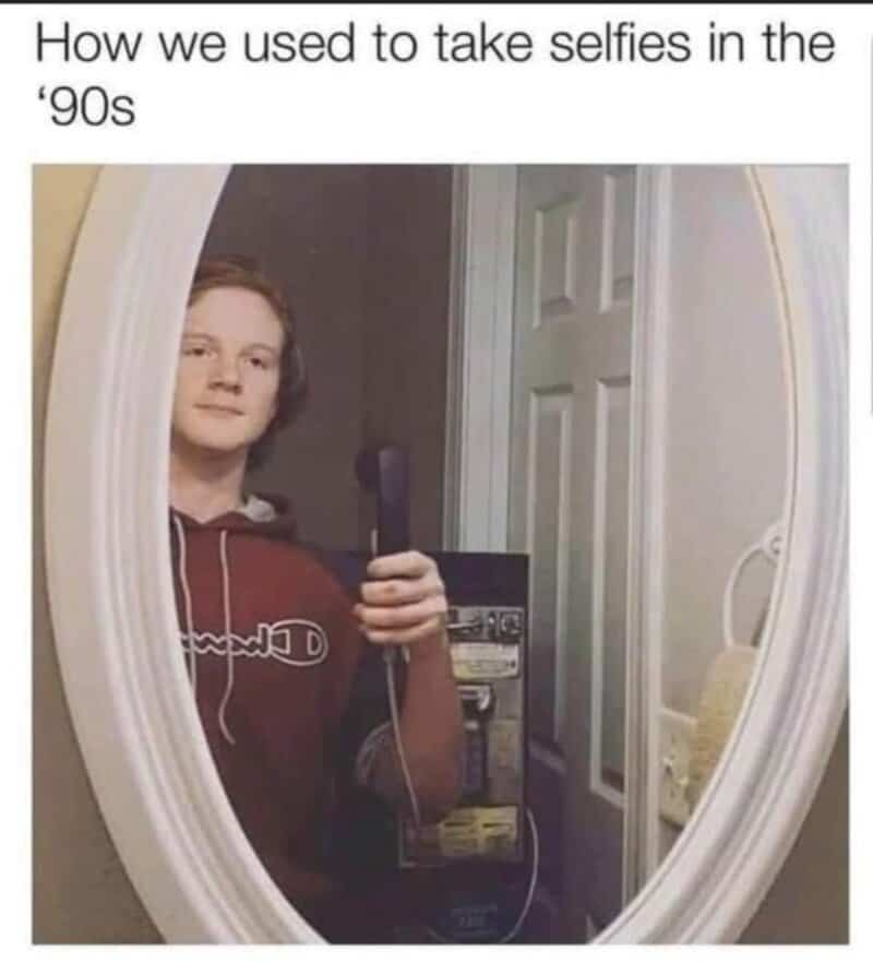 Teen taking a selfie in a mirror with a phone, wearing a hoodie, 90s style.