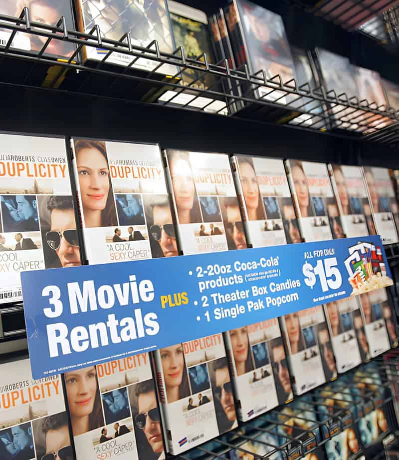 Display of movie rentals with a promotional sign for 3 movie rentals for $15.