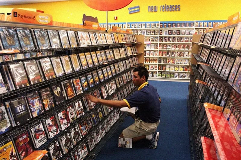 A man shopping for video games in a store aisle with shelves full of games.