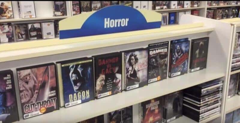 DVDs of horror movies on a store shelf under a 'Horror' sign.