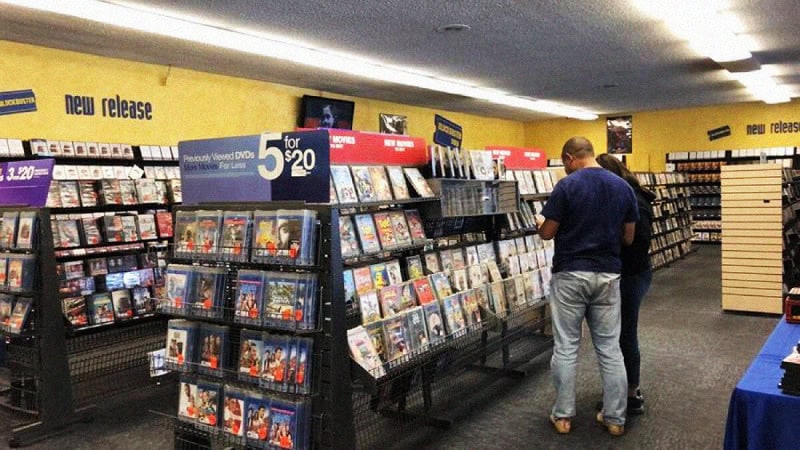 A man shopping for DVDs in a store with shelves filled with movies.