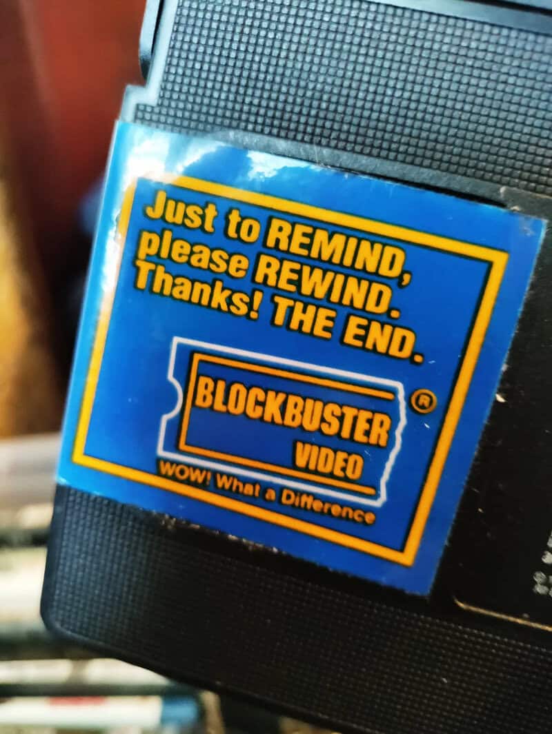 Close-up of a VHS tape with a label that says 'Just to REMIND, please REWIND. Thanks! THE END.' and.