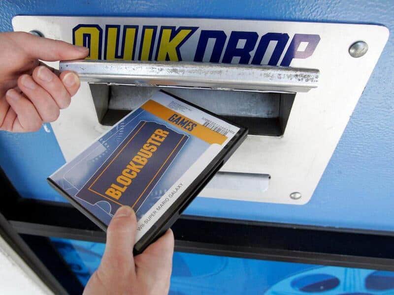 Person inserting a DVD titled 'Blockbuster' into a vending machine.